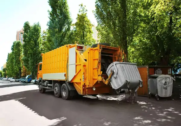 a yellow trash truck parked on the side of a road.