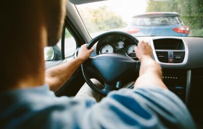 A man sitting in a car with hands on the steering wheel while driving on the road.